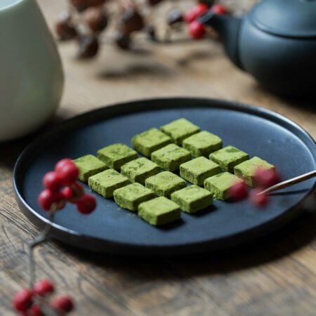 Matcha nama chocolate on a black plate with a Japanese teapot